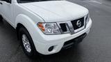 A white 2016 Nissan Frontier with a chrome grille and silver wheels parked in a wet area