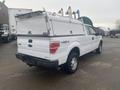 A white 2013 Ford F-150 pickup truck with a cap on the bed and 4x4 designation visible on the rear tailgate