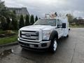 A white 2016 Ford F-550 with utility features and yellow lights on the roof parked in a lot