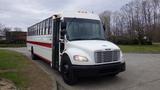 A 2013 Freightliner M2 106 bus with a white body and red stripe parked at an angle with large windows and a black front bumper