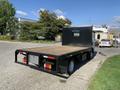 A 2015 Isuzu NPR truck with a flatbed and a black rear wall featuring vents