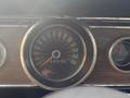A close-up view of a vintage 1966 Ford Mustang dashboard displaying the speedometer and gauges with a wooden finish