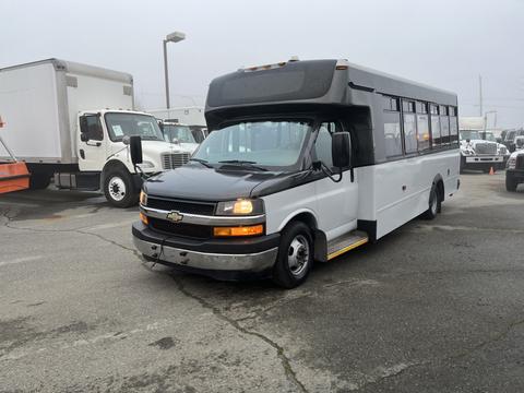 A 2017 Chevrolet Express bus with a black front and white body parked in a lot