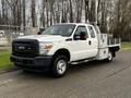 A white 2014 Ford F-250 SD pickup truck with a flatbed and tool compartments on the sides