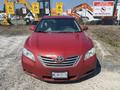 A red 2007 Toyota Camry Hybrid parked prominently with its front view visible showcasing the Toyota emblem and hybrid designation on the grille