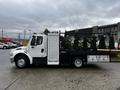 A white 2005 Freightliner M2 106 truck with a flatbed and equipment mounted on the back parked on a concrete surface