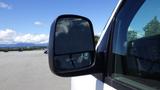 Side mirror of a 2015 GMC Savana with a clear reflection of clouds and sky visible in the glass surface