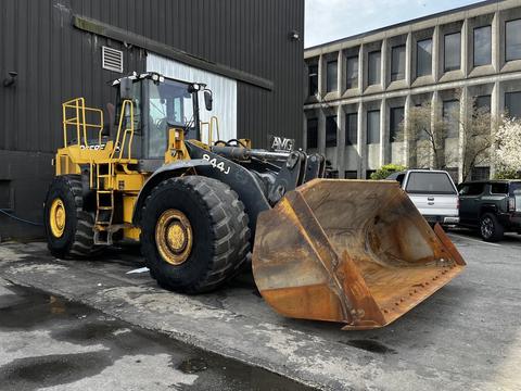 A yellow 2006 John Deere 470G wheel loader with a large bucket at the front and large tires parked beside a building