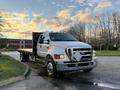 A 2006 Ford F-650 flatbed truck with a silver exterior and a distinctive diamond-shaped grille parked at an angle with a flat cargo area behind the cab