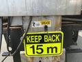 A 2010 Ford F-550 truck with a warning sign that reads "KEEP BACK 15 m" and a grease caution label