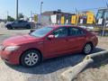 A red 2007 Toyota Camry Hybrid parked on gravel showing its profile with four doors and alloy wheels