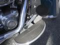 A close-up view of a Harley-Davidson motorcycle footpeg and engine components showcasing chrome and textured surfaces