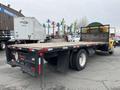 A yellow 2007 International 4300 flatbed truck with a wooden deck and dual rear wheels is parked with its back facing the viewer