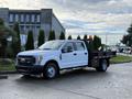 A white 2017 Ford F-350 SD with a flatbed and rear construction-style rack parked on a roadway