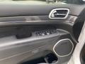 Interior view of a 2018 Jeep Grand Cherokee door panel featuring control switches for windows and mirrors along with a speaker and carbon fiber accents