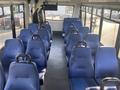 Interior of a 2018 Chevrolet Express showing blue upholstered seats arranged in rows with a central aisle and a monitor mounted on the front wall