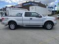 A silver 2013 Ford F-150 with a crew cab and chrome wheels parked in an industrial area