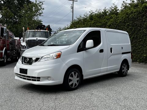 A white 2020 Nissan NV200 van is parked with its side door slightly open showcasing its compact design and commercial utility features