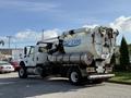 A white 2013 International 7400 vacuum truck featuring a large tank and hoses attached to the rear with the label "VACTOR 2100" on the side