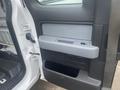 Interior door panel of a 2013 Ford F-150 featuring a textured gray armrest and a handle along with storage compartments below