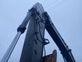 A 2014 John Deere 350G excavator arm with hydraulic cylinders and hoses extending upward against a cloudy sky