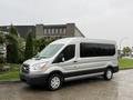 A silver 2019 Ford Transit van with a high roof and large windows parked on a wet road