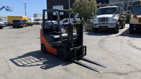 A 2018 Toyota 8FGCU25 forklift with a black frame and orange accents equipped with two metal forks for lifting and transporting materials