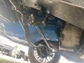 Underneath a 1966 Ford Mustang showing engine components and a blue-painted engine block with various metal fittings and tubes