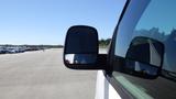 A 2012 GMC Savana van with a focus on the side mirror showing a reflection of the other vehicles in a parking lot