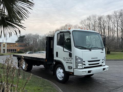 A white 2018 Isuzu NPR truck with a flatbed and side panels facing slightly to the right