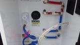 A panel featuring various plumbing connections including a black tank flush system with blue and white hoses and caution labels