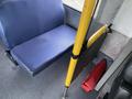 Interior view of a blue bus seat next to a yellow support pole and a red object on the floor