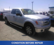 A silver 2013 Ford F-150 pickup truck with a crew cab and black running boards parked in a lot with signs indicating it is in condition before repair