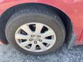 A close-up of a tire and alloy wheel from a red 2007 Toyota Camry Hybrid showing five spokes and a treaded tire with visible wear