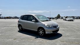 A silver 2006 Honda Fit parked on a paved area with a sleek design and alloy wheels