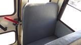 Interior view of a grey vinyl seat in a 2014 International 3000 school bus with a red lever and window beside it