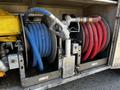 A 2013 Kenworth T370 with two large hose reels one blue and one red mounted on the side showing the ends of the hoses and a fuel nozzle attached to the spray gun