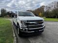 A white 2020 Ford F-250 SD parked with a prominent front grille and hood emblem showcasing its rugged design and chrome accents