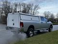 A silver 2012 RAM 3500 pickup truck with a white camper shell in the bed is parked on the roadside with steam rising from the exhaust pipe