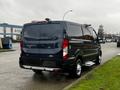 A 2020 Ford Transit van with a dark blue exterior parked on the street featuring sliding side doors and rear windows