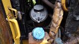 A close-up view of machinery components on a 2019 Caterpillar 972M XE featuring a black cap and a blue valve among various pipes and fittings