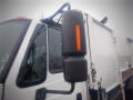 A 2008 International 7400 garbage truck featuring a side mirror with an orange indicator light and a white body with a storage compartment