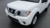 A white 2016 Nissan Frontier with a distinctive grille and rounded headlights positioned at an angle with the front wheels visible