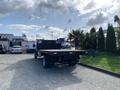 A 2013 Ford F-450 SD truck with a flatbed and black grill parked in a lot surrounded by greenery and other vehicles