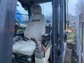 A John Deere 350G excavator seat and controls visible from the cab with a logo on the headrest and joystick lever on the side