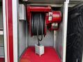 A red hose reel with a black hose coiled neatly inside mounted on a metal panel