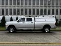 A silver 2012 RAM 3500 pickup truck with a utility cap on the bed parked on a street angle showing its side profile