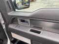 The interior door panel of a 2014 Ford F-150 featuring a chrome handle power window controls and a storage compartment