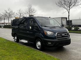 A 2020 Ford Transit van in dark blue parked on a street with trees in the background