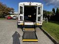 A 2015 Chevrolet Express with a lowered ramp in the back doors positioned for loading passengers or cargo